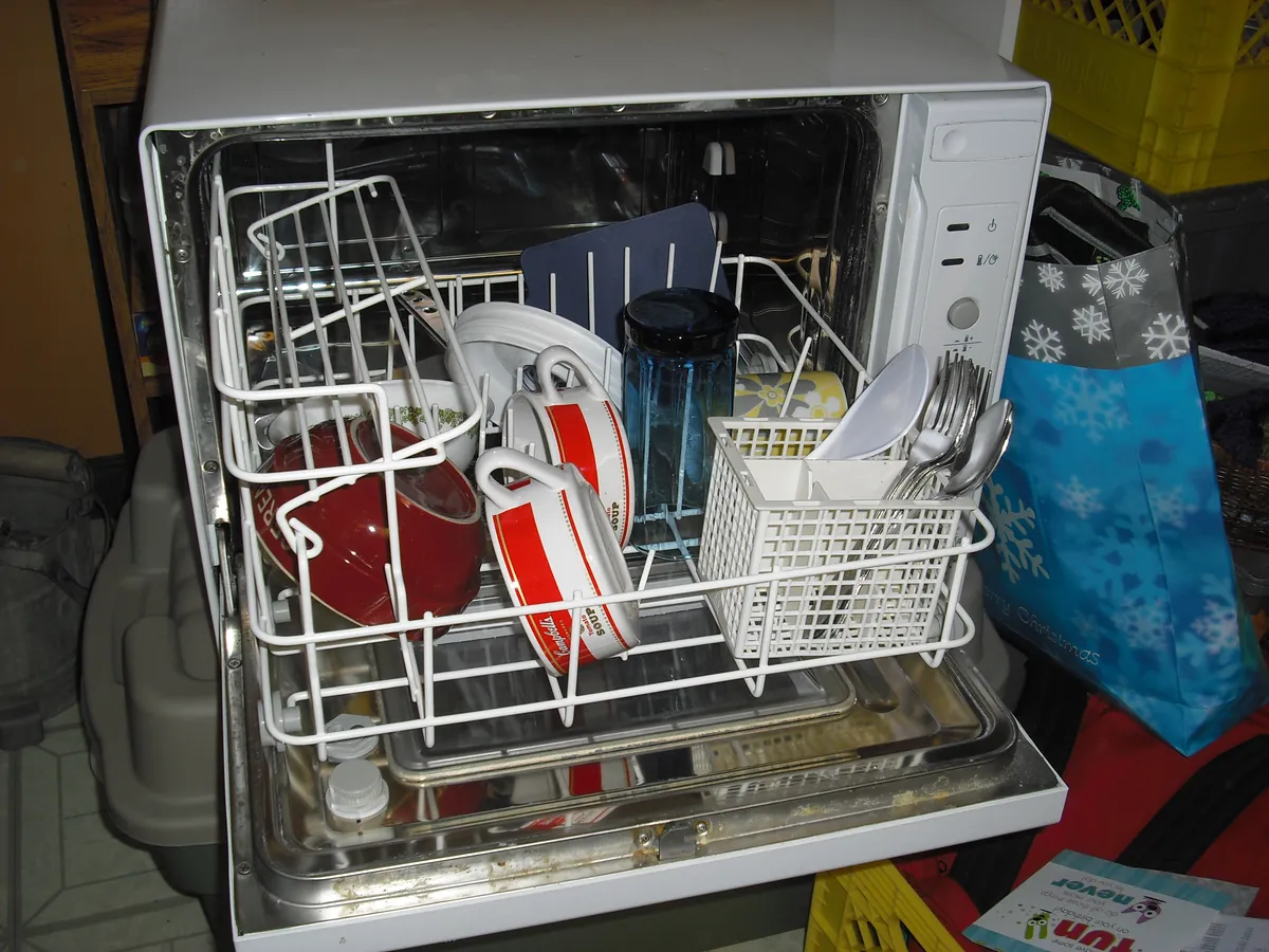 Small dishwasher standing open with plates and a cutlery basket in the racks