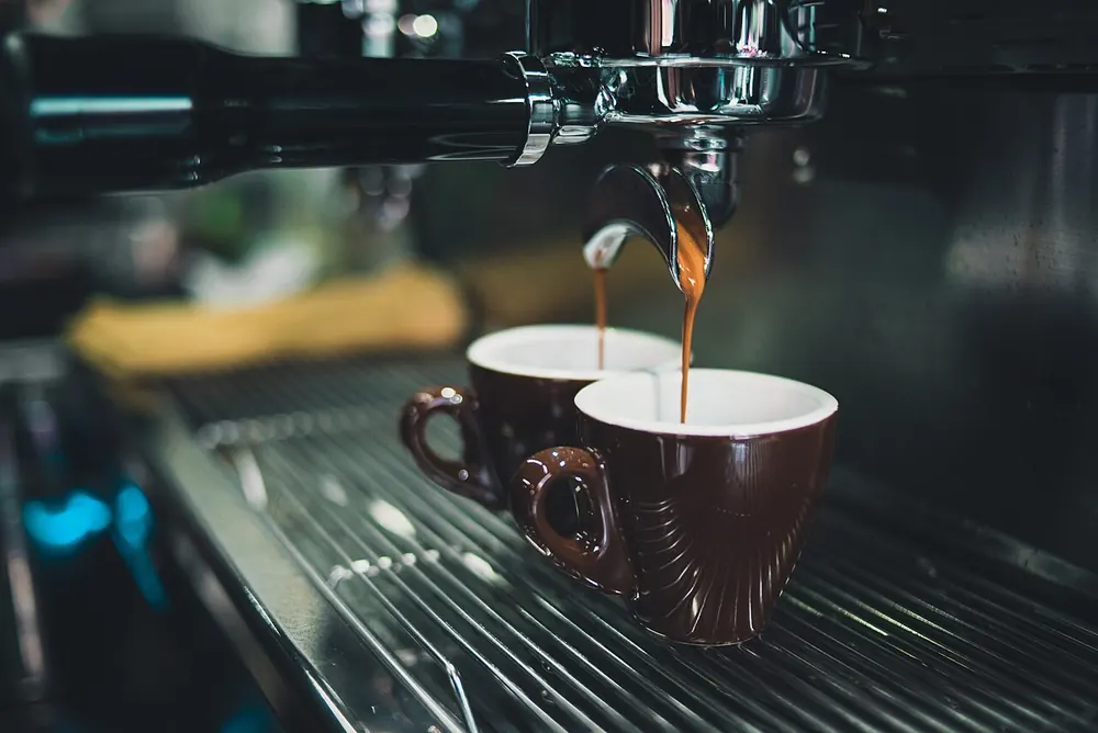 Espresso pouring from a machine into two brown cups