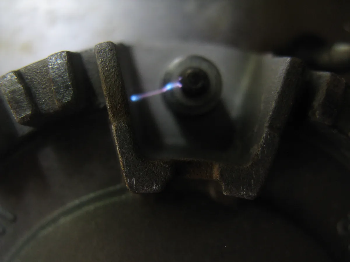 A spark electrode beside a gas burner snapping a small blue arc
