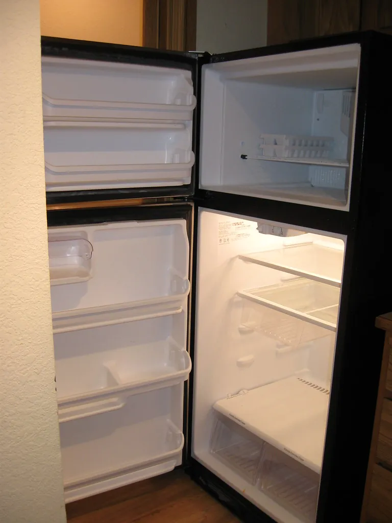 Two-door refrigerator standing open with its shelves empty