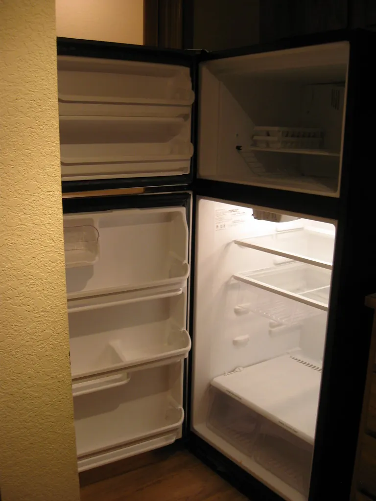 Open refrigerator with empty glass shelves, crisper drawers and door bins