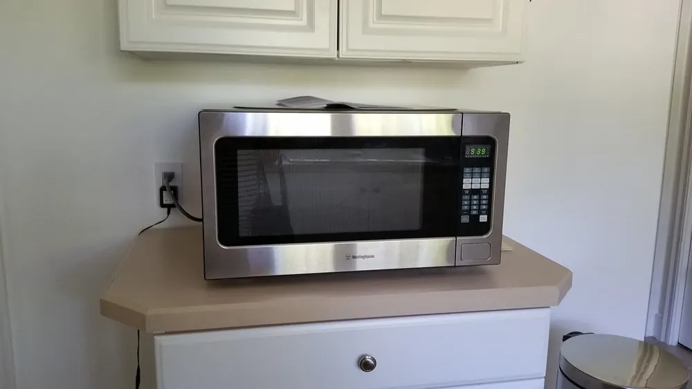 Stainless countertop microwave on a kitchen cart under white cabinets