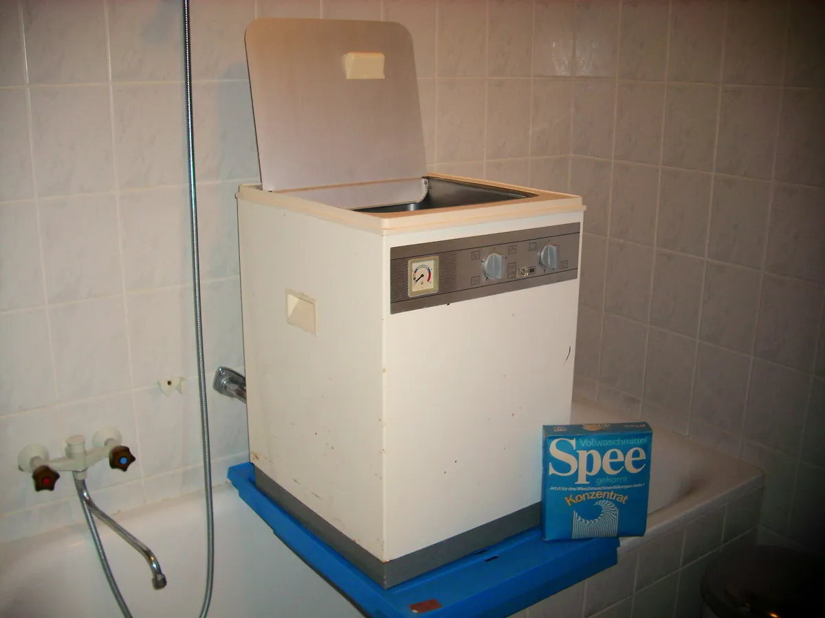 Compact top-load washing machine with its lid raised in a tiled laundry room